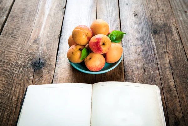 Fruta deliciosa. damascos com um livro sobre um fundo de madeira — Fotografia de Stock