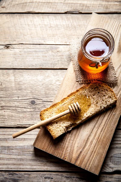 Miel en un frasco, rebanada de pan, trigo en una vieja mesa de madera de tablones vintage . Imagen de stock