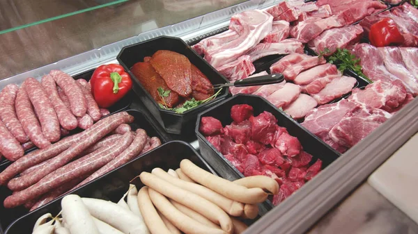 meat department display shelves with selection of typical fresh raw meats slices and variety of sausage products inside market or supermarket refrigerated background.