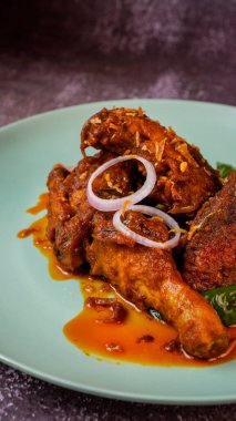 Baharatlı kırmızı körili tavuk soğan halkası ve yeşil biberle süslenmiş..