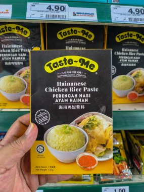 PERAK, MALAYSIA - OCTOBER 22, 2025: Hand holds a box of Taste-Me Hainanese Chicken Rice Paste in a supermarket aisle.