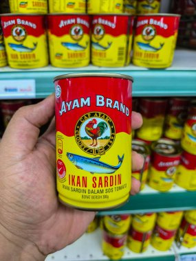 PERAK, MALAYSIA - 22 Ekim 2025: Bir süpermarkette bir kutu Ayam Brand Ikan Sardin 'i domates sosunda tutuyor.