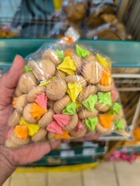 Bir el, parlak renkli şekerli geleneksel buzlu bisküvilerden oluşan şeffaf bir plastik poşet tutar..