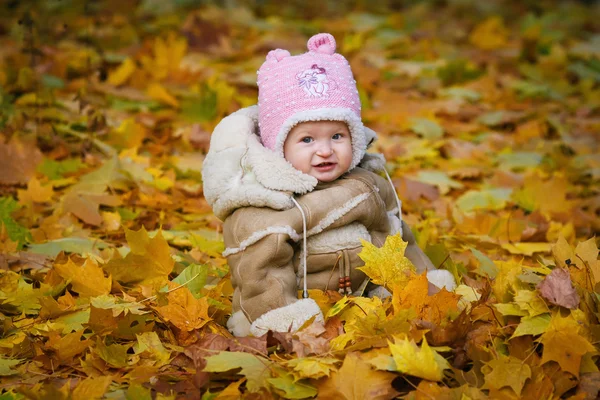 Das Kind sitzt im gelben Laub — Stockfoto