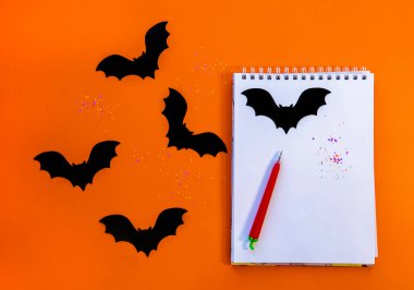 Turuncu arka planda kağıt yarasalar ve kalemli bir not defteri. Yukarıdan görünüşü