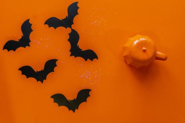 Turuncu arka planda kağıt yarasalar ve seramik bir balkabağı. Yukarıdan görünüşü