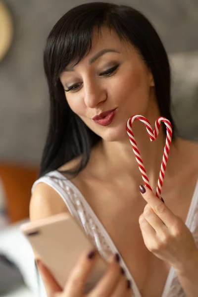 A brunette girl talks via video link, sends a kiss and holds a heart candy in her hands