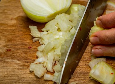 Ahşap doğrama tahtasındaki keskin bir bıçakla organik kahverengi soğanları (allium) doğrayan bir şefe yakın durun..