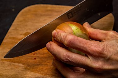 Bir şefin organik kahverengi soğanı (allium) tahta kesme tahtasıyla keskin bir bıçakla doğramasına yakın durun..