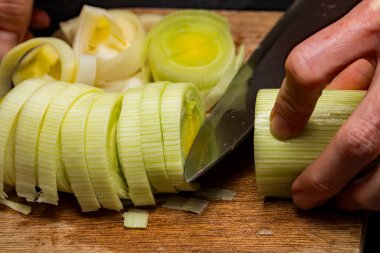 Bir şefin taze organik pırasa (allium ampeloprasum) hazırlarken tahta kesme tahtasının üzerinde keskin bir bıçakla yakın plan.