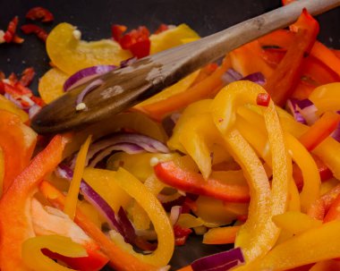 Dilimlenmiş kırmızı soğan (allium cepa), doğranmış kırmızı biber (capsicum) ve sapsız bir tavada doğranmış sarı biber.