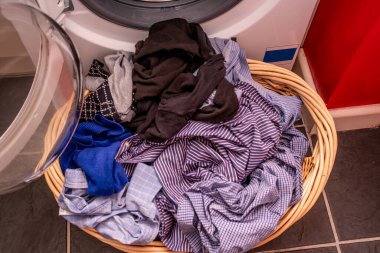 Çamaşır makinesinin önünde bir sepet dolusu ıslak çamaşır.