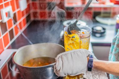 Plastik testiyi sıcak havuç, zencefil, kırmızı soğan ve sarımsak ile dolduran ev aşçısının seçici odağı sağlıklı ev yapımı çorbaya karışmaya hazır.