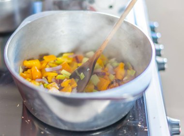 Sağlıklı ve besleyici bir vejetaryen kırmızı biber güveci yapmak için paslanmaz çelik tenceredeki kırmızı soğan ve sarımsağın seçici odak noktası.