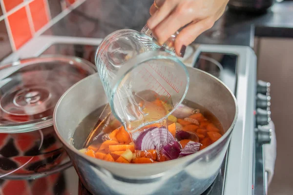 Bir ev yemeği şefinin seçici odak noktası bir tabak doğranmış havuç, zencefil, kırmızı soğan ve sarımsak sosuna stok doldurması ve sağlıklı bir ev çorbası yapması.