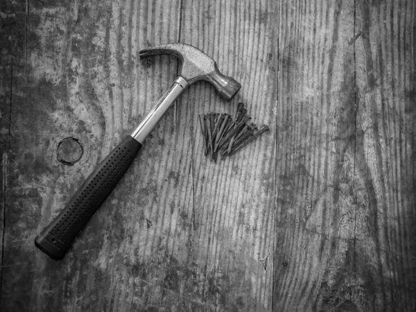 Pençe çekicinin siyah beyaz fotoğrafı ve tahta zeminde paslı çivi yığını.
