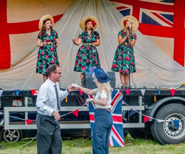 Holt, Norfolk, İngiltere - 14 Eylül 2019. 1940 'ların tarzında dans eden bir çiftin illüstrasyon fotoğrafı. Bir kadın vokal grubu her yıl Holt' ta 40 'ların hafta sonlarına kadar giriş ve çıkış yapabilmek için şarkı söylerken.