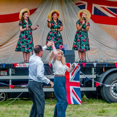 Holt, Norfolk, İngiltere - 14 Eylül 2019. 1940 'ların tarzında dans eden bir çiftin illüstrasyon fotoğrafı. Bir kadın vokal grubu her yıl Holt' ta 40 'ların hafta sonlarına kadar giriş ve çıkış yapabilmek için şarkı söylerken.