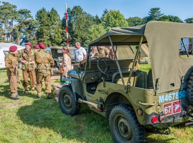 Holt, Norfolk, İngiltere - 14 Eylül 2019. 1940 'lı yılların Holt Norfolk' unda 40 'lı yılların her haftasonunda özgürce girip çıkabilmek için askeri bir cipin etrafında duran 1940' ların tarzında giyinmiş bir grup genç askerin resimli editörlük fotoğrafı.