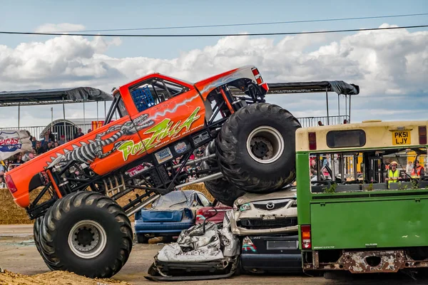 Poddington, İngiltere - 18 Ağustos 2019. Podzilla canavar kamyonunun, bir canavar kamyon gösterisinde kullanılmayan bir otobüsün üzerinden atlamaya çalışırken bir yığın hurda arabaya tırmanmasının resimli bir fotoğrafı.