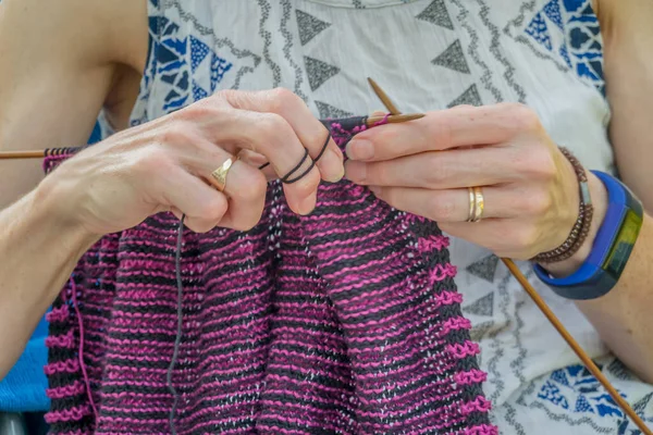 Close up of an unidentifiable lady knitting a stripy cardigan with a pair of wooden bamboo needles