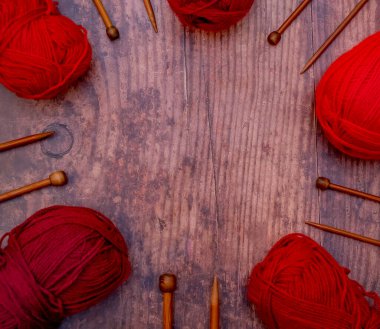 Ahşap bir zeminde kırmızı örgü ipliği ve bambu örgü iğnelerinden oluşan düz toplar.