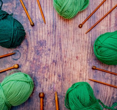 Düz yeşil örgü ipliği topları ve ahşap zeminde bambu örgü iğneleri.