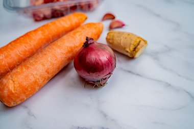 Kırmızı soğanın seçici odağı havuç, zencefil kökü ve sarımsak karanfilli beyaz mermer zemin üzerinde.