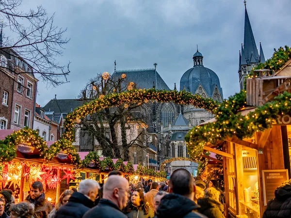 Aachen, Almanya - 07 Aralık 2019. Alacakaranlıkta yoğun bir Aachen Noel pazarının resimli bir fotoğrafı. Kasıtlı olarak arka plana odaklanmış ve kameraya en yakın şenlik düzenleyicileri odak dışı bırakıyor.
