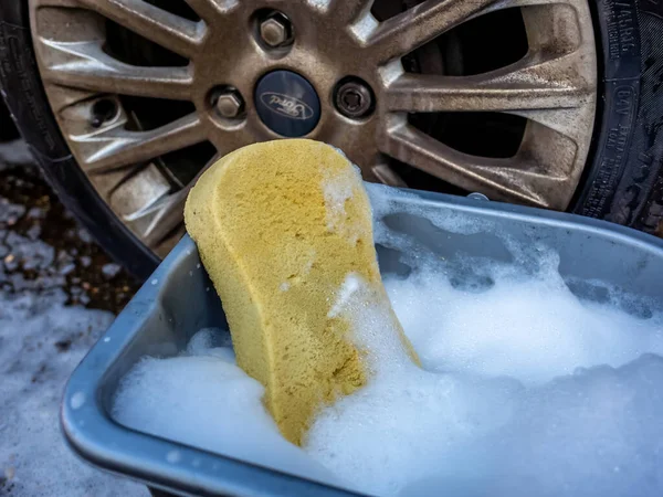 Kirli bir arabanın arka tekerleğinin önündeki sabunlu suyun üzerindeki sarı sünger.