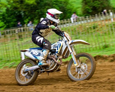 Lyng, Norfolk, İngiltere - 10 Mart 2019. Lyng, Norfolk 'taki Cadders Hill' de İngiliz Motokros Şampiyonası 'nın illüstrasyon fotoğrafı. Yarışçı, önde giden yarışçıları kovalamak için bir tepeye tırmanırken ayağa kalkıyor ve iyi bir ilerleme kaydediyor..