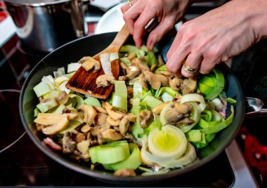 Kimliği belirlenemeyen bir şefin eline odaklanın. Hob 'da pırasa, tavuk ve pastırmalı makarna pişirin.