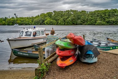 Salhouse, Norfolk, İngiltere - 10 Ağustos 2019. Norfolk 'ta Salhouse Broad' da teknesinde oturan Norfolk Broads Ranger 'la konuşan renkli kanoların yanında duran bir adamın editör fotoğrafı.