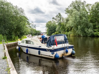 Wroxham, Norfolk, İngiltere - 16 Haziran 2019, Norfolk 'taki Wroxham köyündeki Bure Nehri' nde demirlemiş orta yaşlı bir adamın eğlence gemisini demirlemek için bir yer ararken çekilmiş resmi.