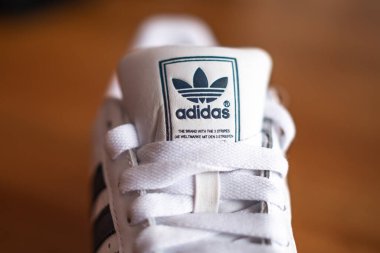 Norwich, Norfolk, İngiltere - Adidas marka beyaz bir spor ayakkabının ahşap bir masanın üzerindeki resimli editör fotoğrafı. Dil üzerine seçici ve keskin bir odaklanma. Sığ alan derinliği ve bokeh.