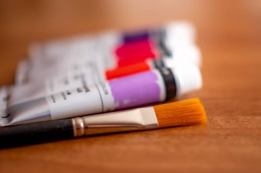 Tahta bir masadaki akrilik boya tüplerinin önündeki boya fırçasını kapat.