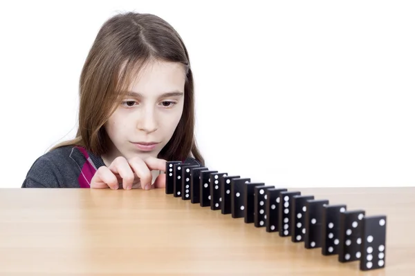 Jeune fille regardant dominos noirs alignés sur panneau en bois isolé sur blanc — Photo