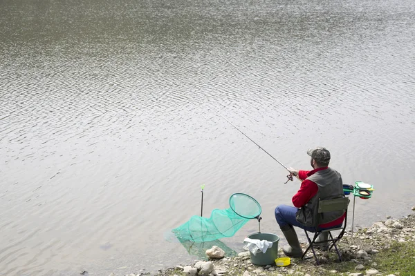 Pêcheur sportif avec équipement de pêche assis sur la côte du lac et la pêche, petites vagues sur la surface de l'eau — Photo