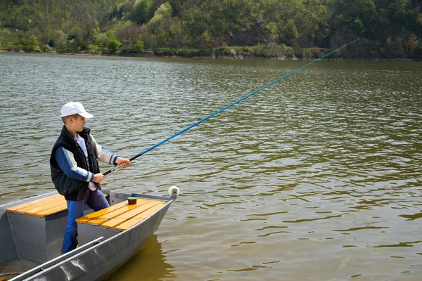 Pequeño niño sosteniendo una caña de pescar y la pesca de barco de madera en el lago — Foto de Stock