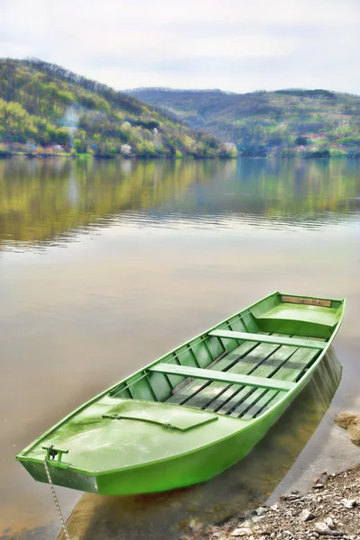 เรือไม้สีเขียวผูกพันกับท่าเรือเล็ก ๆ บนทะเลสาบสงบ — ภาพถ่ายสต็อก