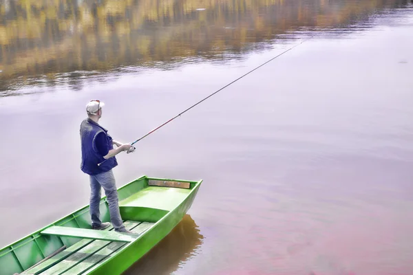 Rybak Casting wędkę z zielonych łodzi na jeziorze i cierpliwie czekam na ryba połknie przynętę — Zdjęcie stockowe