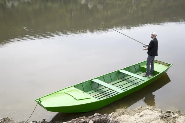 Pescador deportivo sosteniendo caña de pescar y pesca desde el barco verde — Foto de Stock