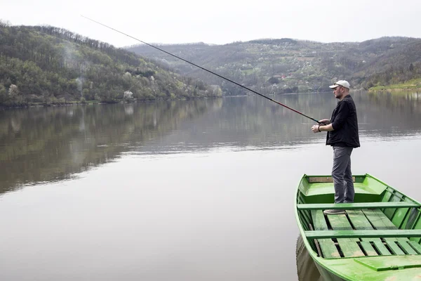 Vista lateral del deporte pescador con gorra y chaleco de pesca de la canoa verde y disfrutar de sus vacaciones — Foto de Stock