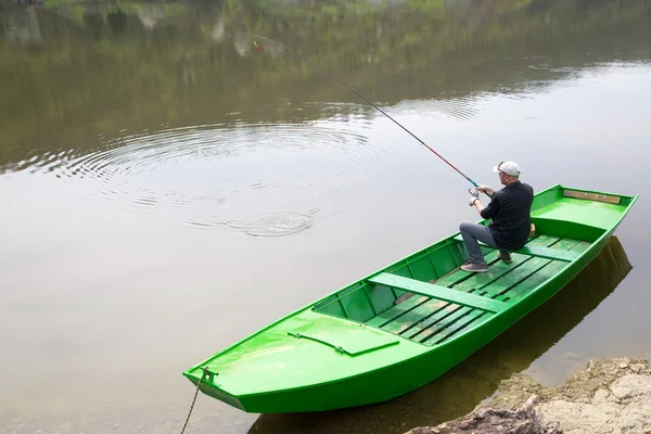 Man Wearing Cap And Vest Sitting In Green Rowboat And Fishing On The River — Stock Photo, Image