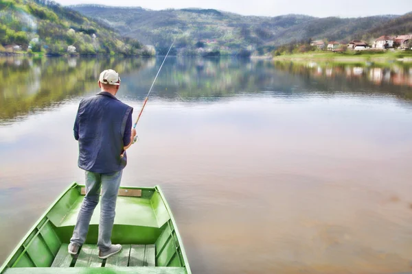 Homme debout sur un bateau vert avec son dos vers la caméra et la pêche sur le lac calme — Photo