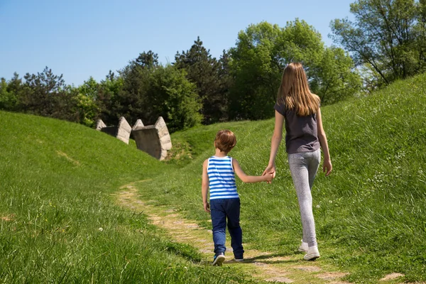 Hátulnézet, testvére és a húga gazdaság kéz és a séta a parkban, élvezheti a napos Tavasz — Stock Fotó