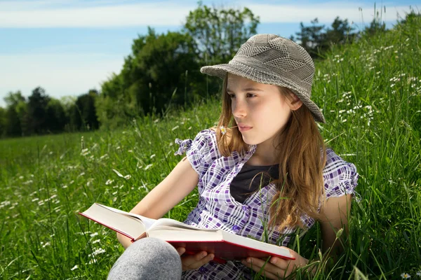 Primer plano Retrato de una joven pensativa con libro en sus manos sentada en la hierba en la ladera y mirando pensativamente hacia los lados —  Fotos de Stock