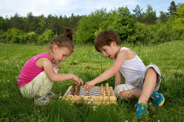 Kisfiú és a lány ül a fűben és a tanulás, hogyan kell játszani sakk, a szép tavaszi napon — Stock Fotó