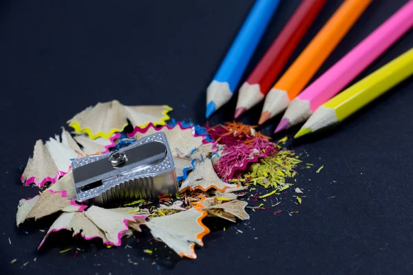 Nabroušené barevné tužky pocházející z rohu, kovové ořezávátko a barevné tužky hobliny na černém pozadí — Stock fotografie