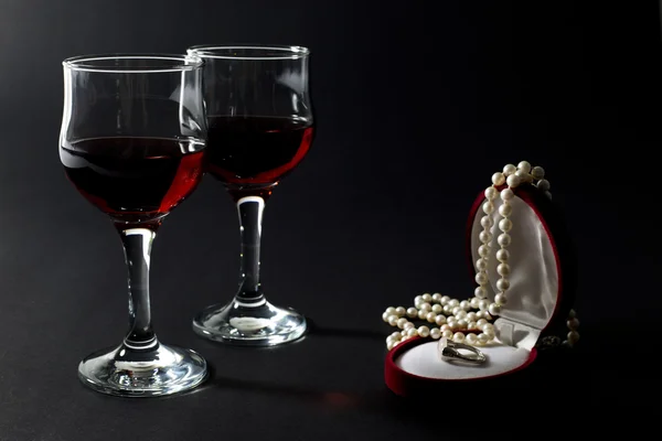 İnci kolye ve takı kutusunda siyah izole kırmızı şarapla dolu iki kadehlerin ile altın yüzük — Stok fotoğraf